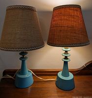 Pair of turquoise bedside lamps on table, showing full view of bases and shades