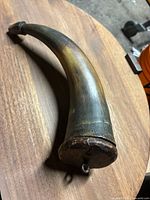 Side view of the curved powder horn showing natural horn coloration and wooden stopper at the end.