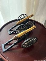 Two vintage die cast Revolutionary War field cannon models displayed on a wooden surface showing overall size and design.