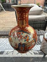 Front view of the vintage Japanese Satsuma vase showing detailed hand-painted floral and architectural scene with gold gilded embellishments on a red crackle glazed background.