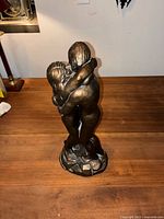 Front view of the Adam and Eve embracing sculpture on wooden surface.