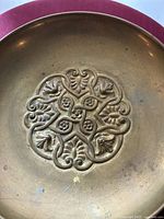 Close-up photo of the ornate central medallion on the brass dish, highlighting fine details of the embossed foliage and stylized animal heads.