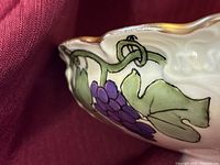Close-up of the grape and vine hand-painted design and gold rim on the bowl's edge.