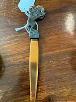 Close-up photo of the letter opener showing the bronze bronco head handle and copper blade lying on a wooden surface.