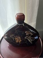 Front angled view of dark stoneware tequila decanter featuring engraved images of wild horses and a round wooden stopper.