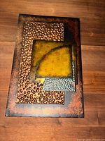 Full top-down view of the sculpture showing layered rectangular metal panels with different textures and copper, green and blue patina finishes