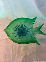Top view of the emerald green fish-shaped Venetian Murano glass bowl showing the blue sunburst center pattern and curved fin details.