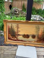 The oil painting landscape shows a lake with forested islands and colorful trees framed in an ornate gold frame.
