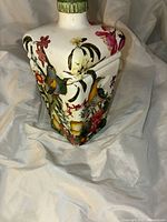Overall view of the porcelain art bottle on fabric showing floral and bird painted details on one side