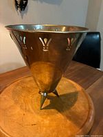 Champagne cooler with chromed metal finish, tripod legs, and cut-out pattern, placed on a wooden surface.