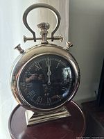 Front view of a polished stainless steel vintage mantle clock with black dial and white Roman numerals.