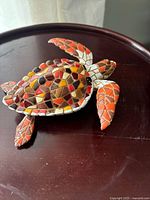 Top angle view of hand-painted sea turtle sculpture showing mosaic tile shell in amber, rust, brown, and cream colors.