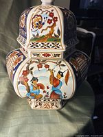 Side view of vase showing floral motifs, branches, and figures in traditional dress in vibrant multi-colors on white porcelain with gold and blue accents.
