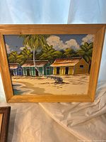 Frontal image of one vintage painting depicting colorful tropical beach huts with palm trees and sandy beach in wood frame.