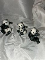Three vintage ceramic panda bear figurines displayed on white fabric background. Each panda has a glossy black and white painted finish and plays with a cub in a different pose.