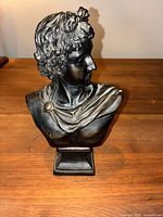 Front view of black bust sculpture showing facial details and hair curls resembling classical Apollo statue.