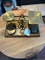 Front view of vintage postage scale on wooden base showing brass circular and rectangular platforms and five brass weights.