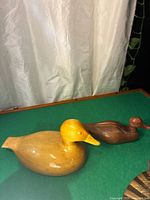 Two handcrafted wooden duck decoys placed on a green surface with a light background, showing the size, shape and color tones of each decoy.