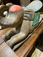 Close-up side angle of vintage hand carved wooden elephant rocking toy showing the red saddle cushion and green details on the side, mounted on curved wooden rocking base.