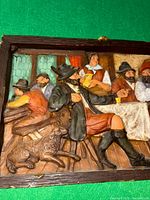 Close-up view of wax picture showing seated men in period clothing, hat, boots, and a dog on a wooden floor inside a pub.