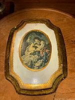 Front view of vintage Florentine wood plaque with ornate gold leaf frame and oval Empire style painting of a couple.
