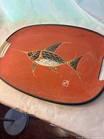 Top view of rectangular vintage mid-century platter with swordfish motif on orange background with black trim and handles.