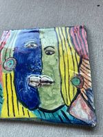 Front angled view showing the colorful hand-painted tile with glossy overglaze and indentations in facial features