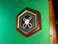 Photo of a hexagonal wooden sailor's box with glass top displaying a white rope sailor's knot on a blue velour background.