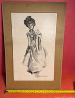 Framed pencil drawing of a woman in period dress signed by Howard Chandler Christy, mounted on tan mat board with a ruler showing approximate size.