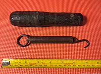 Top-down view of the vintage cast iron spring scale, showing the hook and ring ends alongside a yellow measuring tape indicating approximately 7 inches in length.