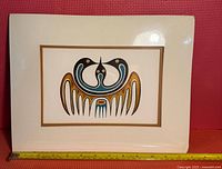 Framed print of Indigenous art with two stylized birds in traditional colors, white mat board with gold trim.