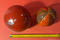 Two spherical Japanese tea caddies on a red mat with measuring tape for size reference.