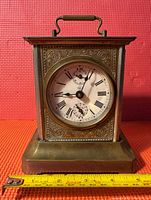 Front view of Junghans brass carriage clock showing Roman numeral dial, music box keyhole, and ornate etching.