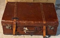 Closed view of the brown leather suitcase with strapping and latches.