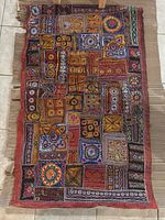 Full view of the rectangular tapestry showing the intricate embroidered patchwork style with various geometric and decorative designs in multiple colors on dark fabric with reddish border trim.