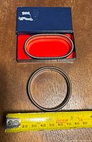 Circular metal sleeve garter placed on wooden surface next to measuring tape showing approximate 6.5 cm diameter