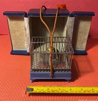 Front view of brass cage on blue base with orange cord and measuring tape showing width