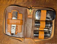 Open grooming kit displaying comb, small containers, and case inside brown leather zippered case