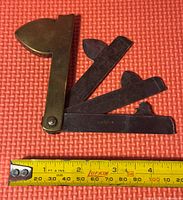 Antique antique bloodletting tool with brass handle and foldable steel blades next to a measuring tape showing length about 3.5 inches