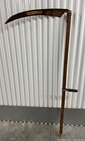 Full photo of vintage scythe showing wooden handle, curved blade, and hand grip.