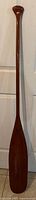 Full length front view of the wooden oar showing its entire shape and paddle blade.