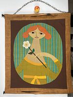 Front view of patchwork textile art depicting red-haired woman holding a daisy, hung with chain and rods.