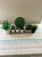 Front view of all six artificial plants positioned on the wooden tray, showing variety of types and pots