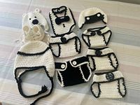 Full view of all 11 crocheted baby items arranged on a striped surface including hats, bib, diaper covers, booties.