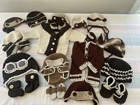 Overhead view of all 26 brown and cream crocheted baby items including hats, booties, mittens, and cardigans spread on white surface.