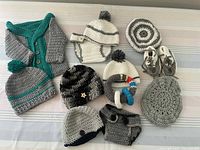 All 13 crocheted baby items laid out on table showing variety of hats, sweater, booties, rattle, and other pieces