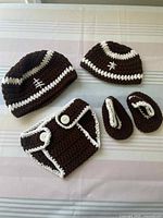 Top down view of two crocheted brown and white baby hats, one diaper cover, and two booties on striped surface.