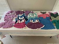 Full view of 33 crocheted baby girl items spread on a table showing dresses, cardigans, and accessories in multiple colors including pink, purple, blue, green, and cream.