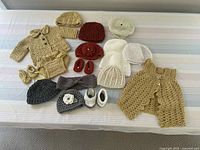 Photo of 20 crocheted baby items displayed, including hats, booties, diaper covers, cardigan, and dress in neutral colors.