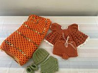 Photo of the full crocheted set including blanket, dress with shorts, hat, diaper cover, and booties laid out on a bed